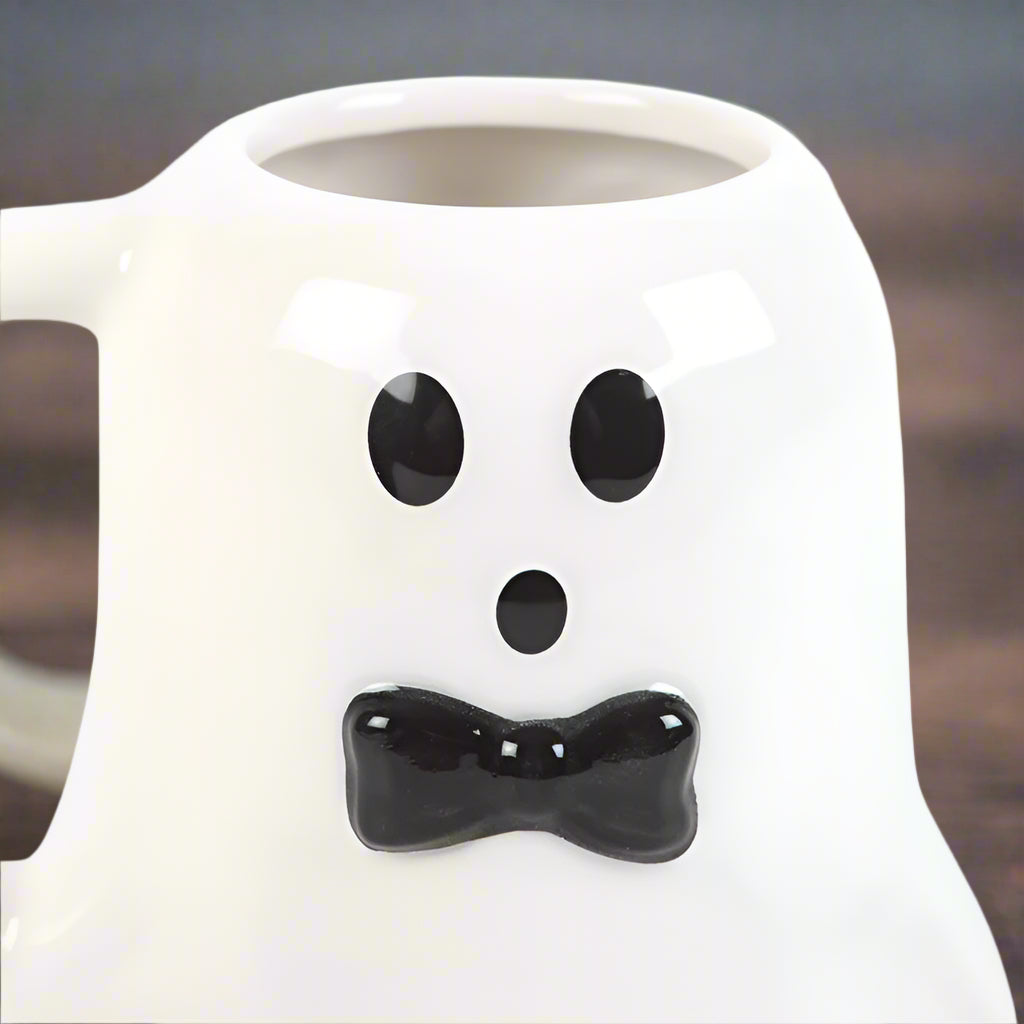 White mug with ghost face design featuring black eyes and bow tie on a white background