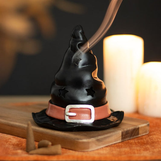 Witch hat incense burner on a wooden board with candles in the background