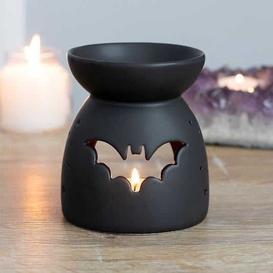 Black ceramic oil burner with bat design on a wooden surface with candles in the background.