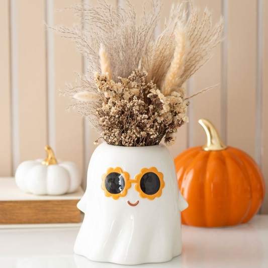 Decorative ghost vase with dried flowers, sunglasses, and pumpkins on a neutral background